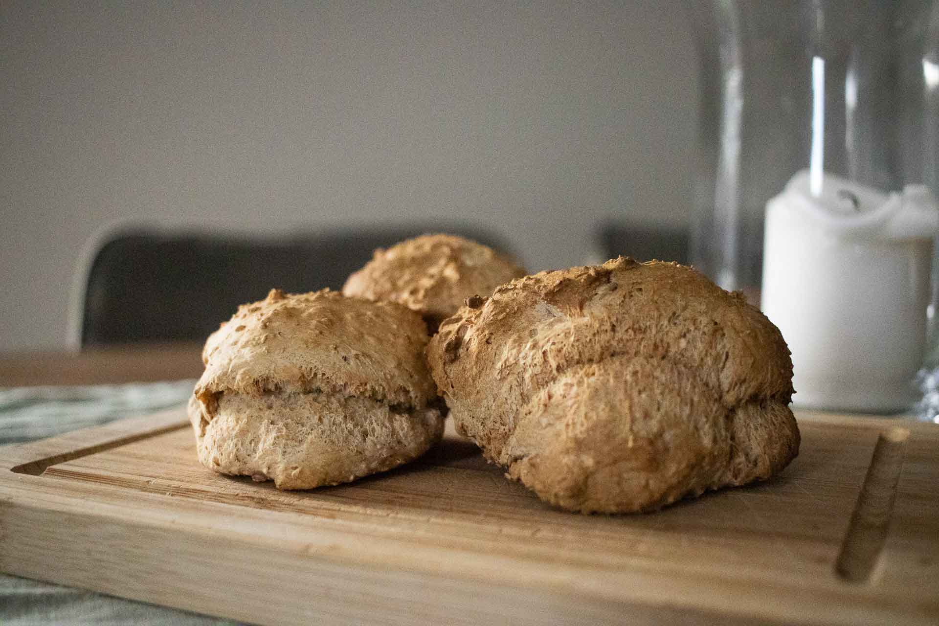 Drei Brötchen auf einem Brett auf dem Tisch, im Hintergrund eine Kerze